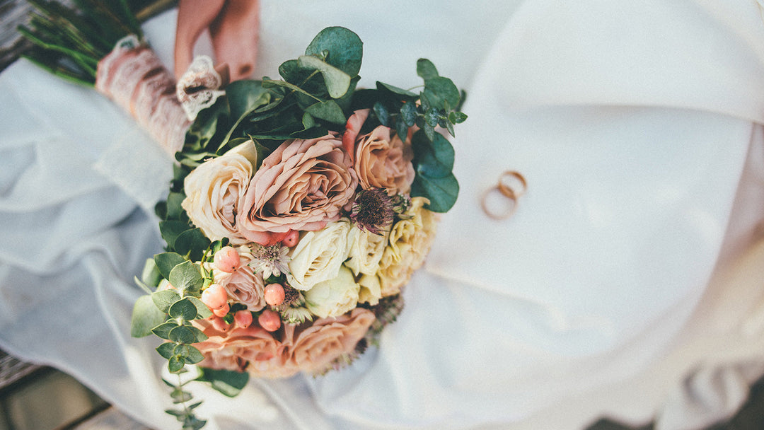 Bridal bouquet with soft roses and wedding rings on a white dress.