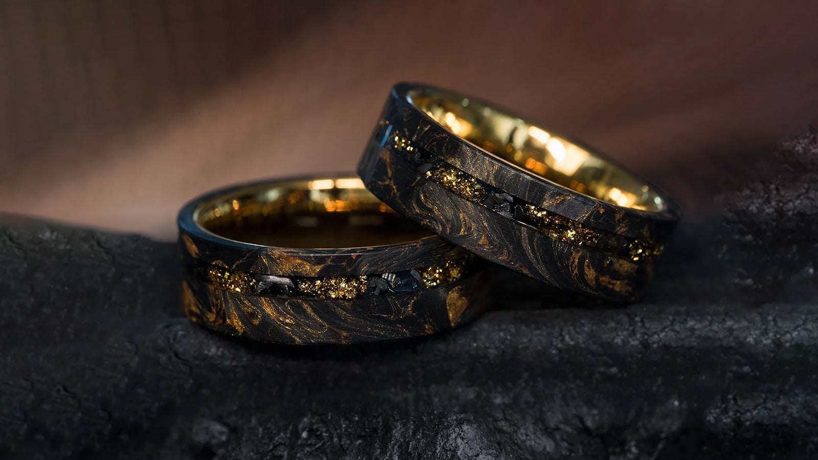 A pair of striking rings with a black and gold marbled resin exterior, a central inlay of gold flakes, and a polished gold inner band