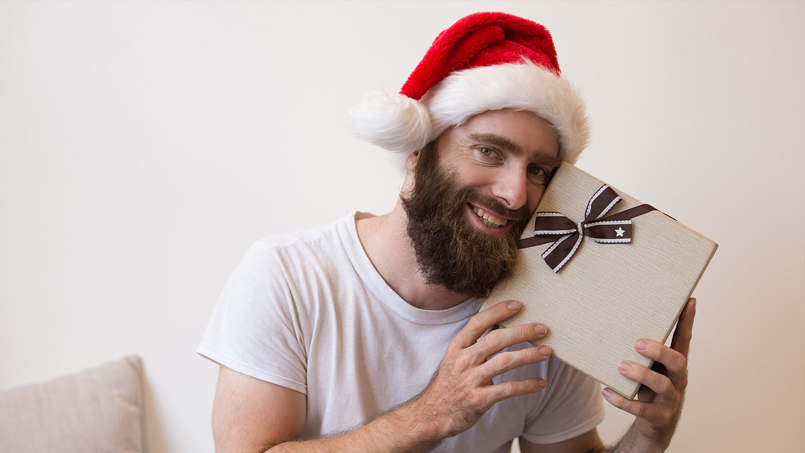 Happy man wearing a Santa hat holding a wrapped Christmas gift box.