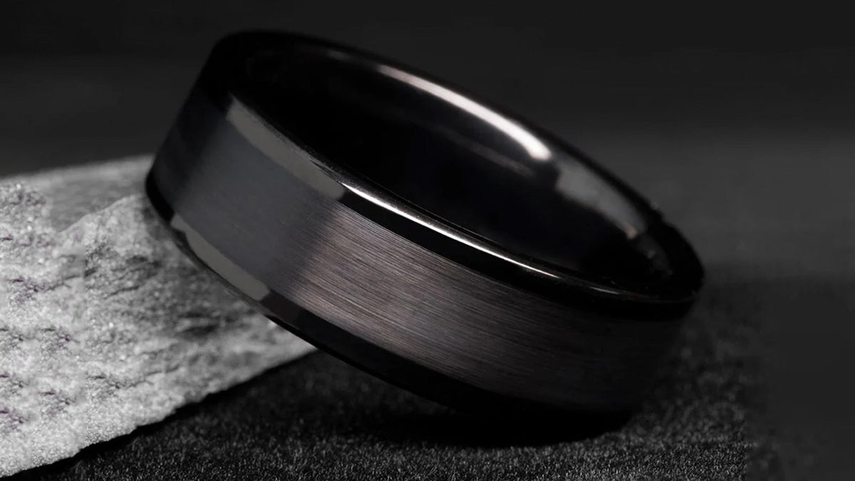 Brushed black ring with polished edges resting on a gray stone against a dark background