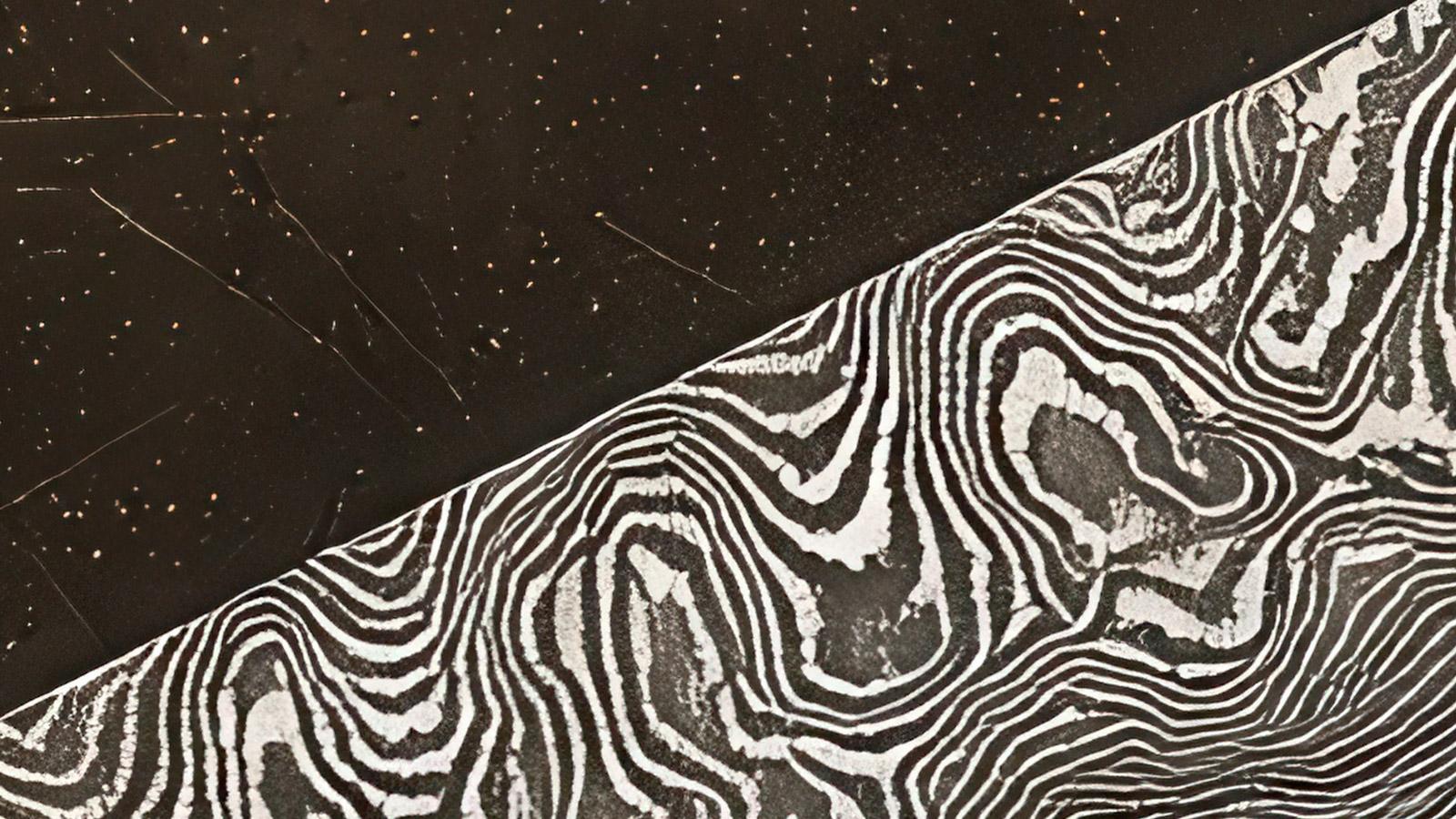 One side features a dark, speckled surface, while the other reveals the intricate, flowing lines of Damascus steel, creating a striking textural contrast.