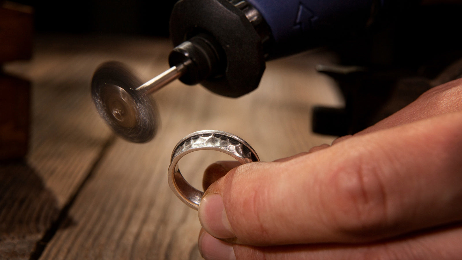 Handcrafting a textured silver ring with a rotary tool on a wooden workbench.