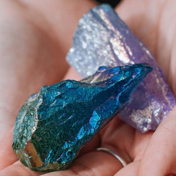 Close-up of person holding raw blue and purple aura quartz crystal specimens