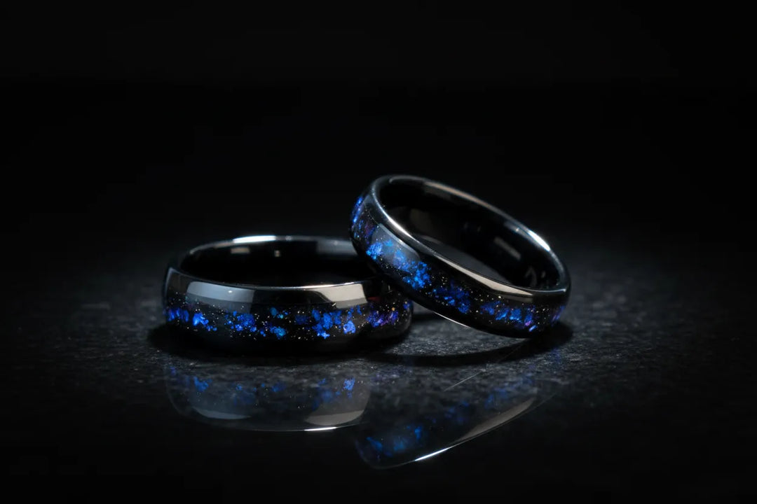 A man's hand wearing a sleek Sagabands comfort fit ring, resting against dark grey textured fabric