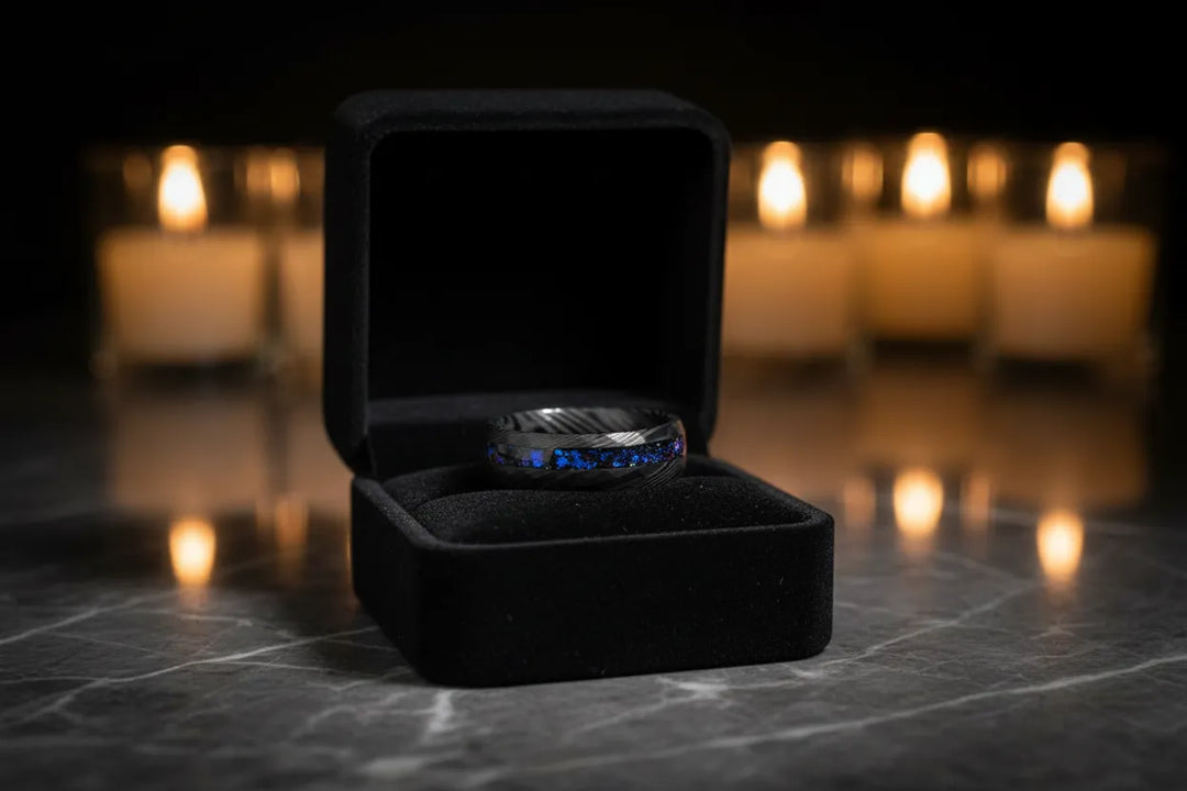 Black tungsten ring with blue sapphire inlay displayed in a black velvet ring box with candlelight background	