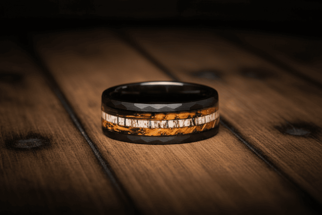 A Sagabands black faceted ring with a textured wood and antler inlay rests horizontally on a dark wooden surface