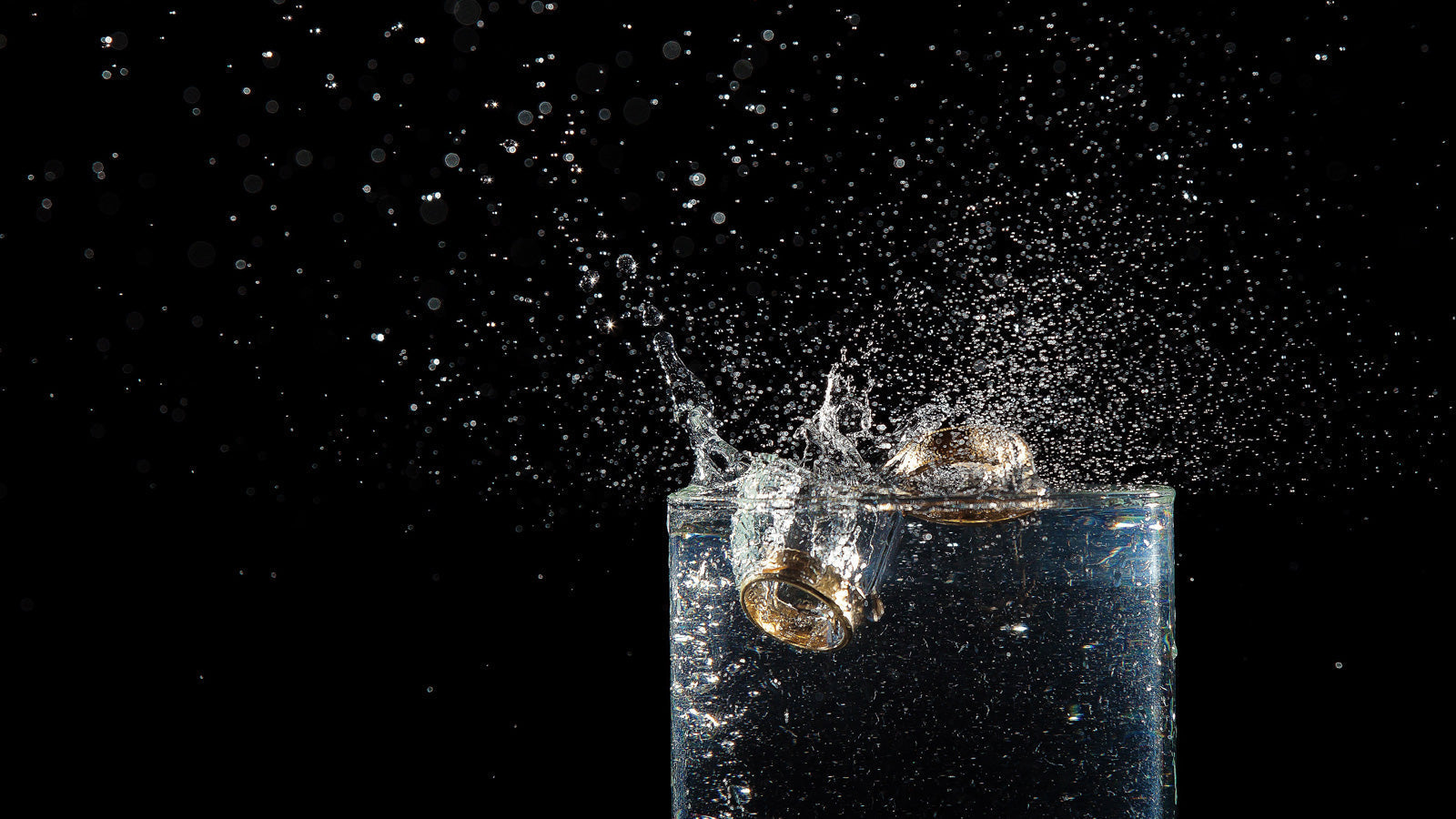 Sagaband gold wedding rings splashing into water glass with flying droplets