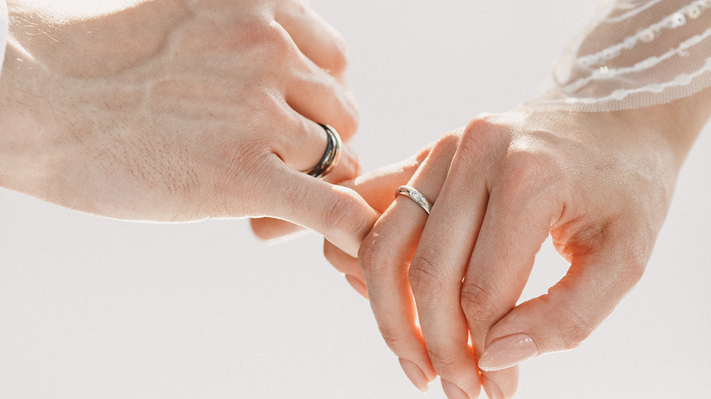 Couple holding hands wearing wedding rings in soft natural light