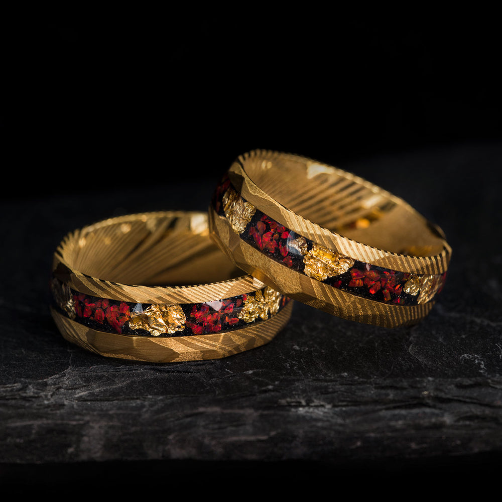 The Red Planet: hammered gold Damascus steel wedding rings with fire opal and gold leaf inlay on dark stone.
