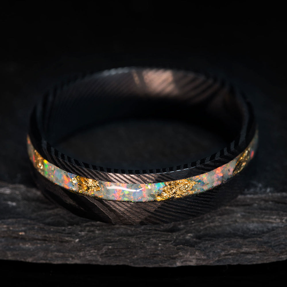 The Eternal Heart wedding ring: black hammered Damascus steel band with a white opal and 22k gold leaf inlay.