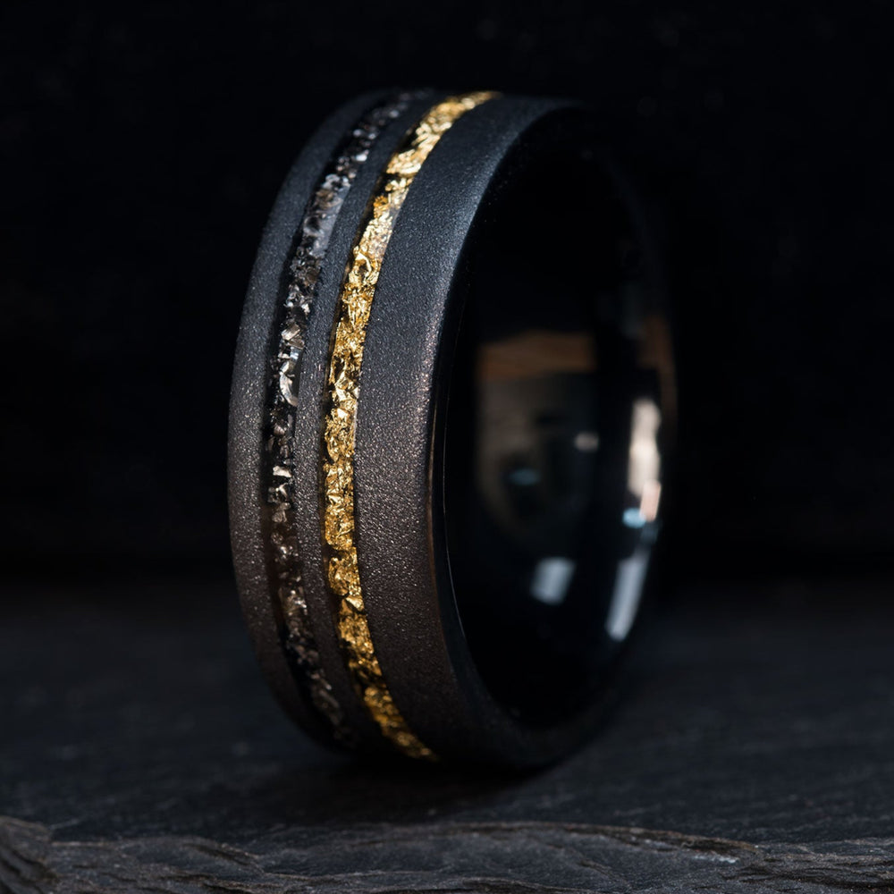 Black sandblasted tungsten carbide ring with Gibeon meteorite and gold leaf inlay on dark background.