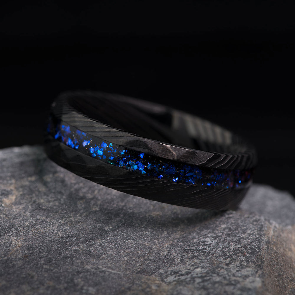 Men's black hammered Damascus steel ring with meteorite and blue alexandrite inlay, unique pattern.