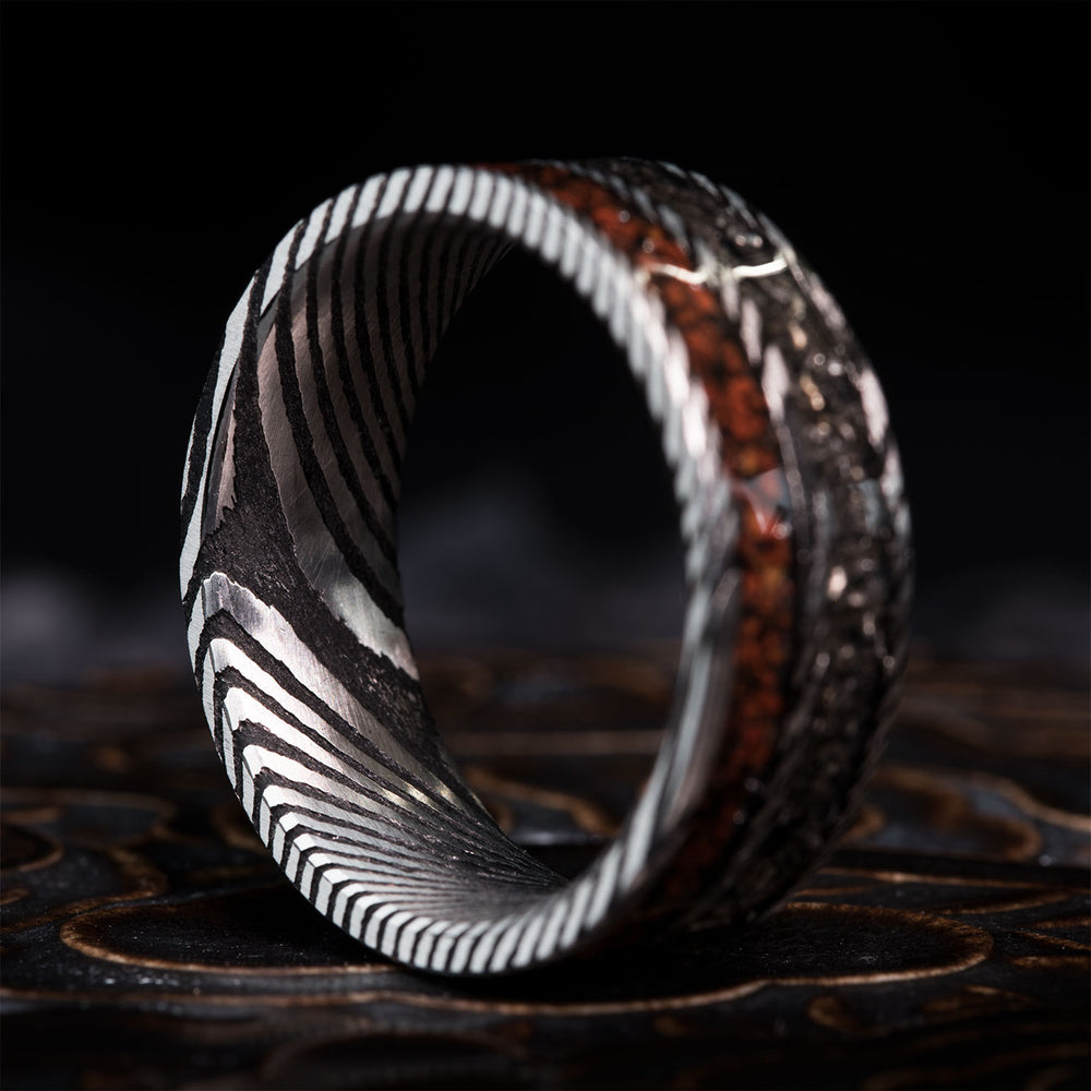 The Evolution ring: silver Damascus steel band with T-rex bone and Gibeon meteorite inlay. Shows product.