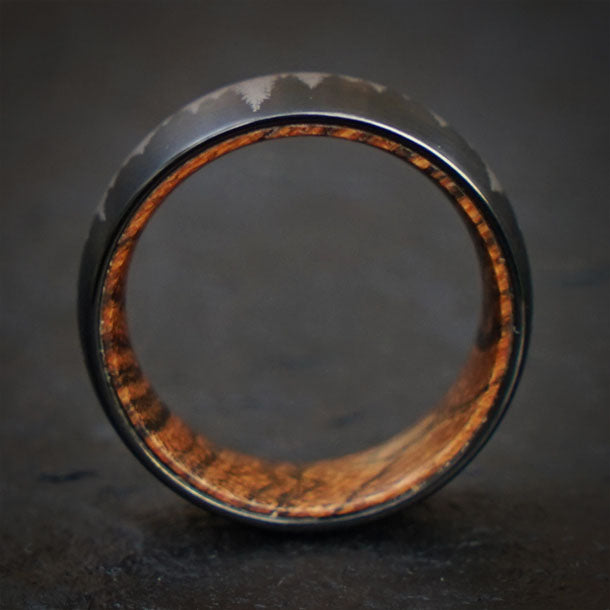 Black tungsten ring with laser-etched mountain detail and natural olive wood interior for product page.