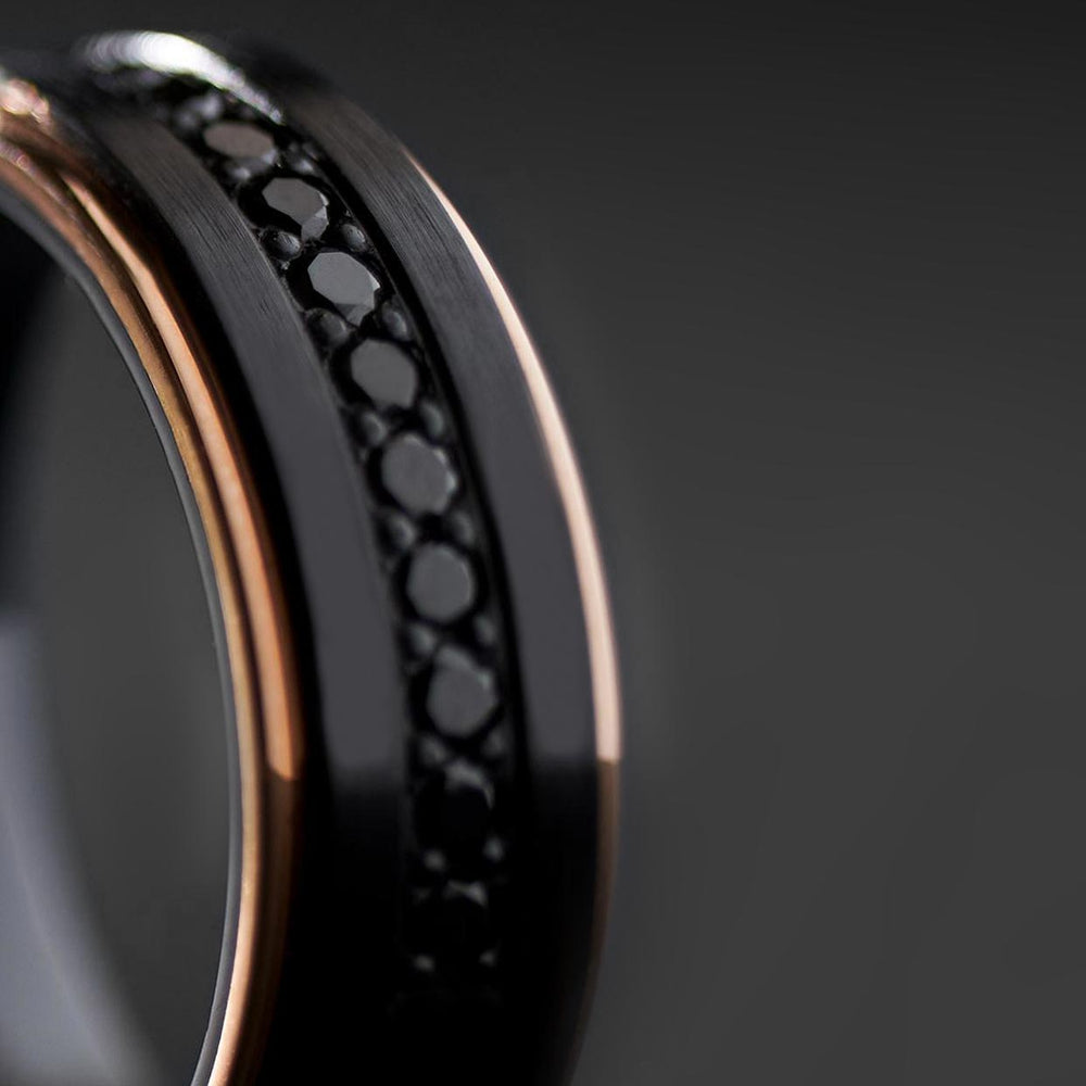 Close-up of men's black tungsten ring with black zircon channel and rose gold edges, product detail view.