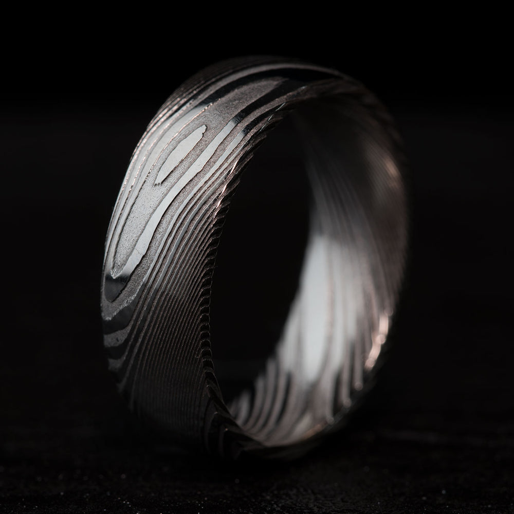 THE SAGE unique Damascus steel ring, 8mm wide, domed comfort fit, showcasing wood-grain swirl pattern.