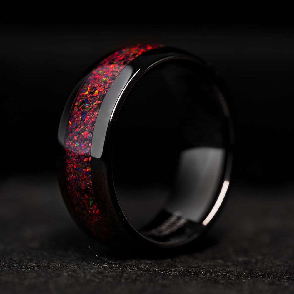 Black tungsten wedding band with a red fire opal inlay, showcasing vibrant iridescent colors. Perfect for product pages.