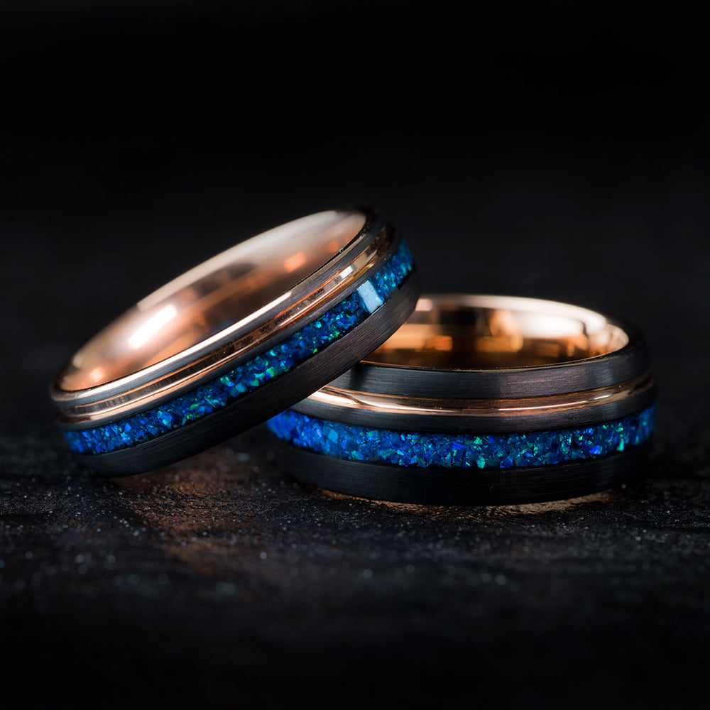 Two black tungsten carbide wedding rings with rose gold inlay and blue opal detail, "The Starshine" couple's set.