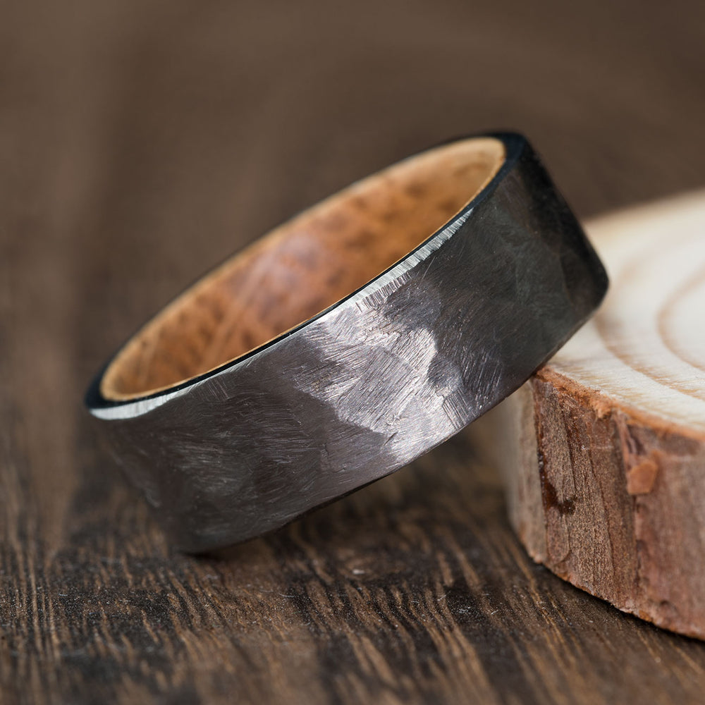 THE TITAN hammered silver titanium wedding ring with whiskey barrel wood inlay on rustic background.