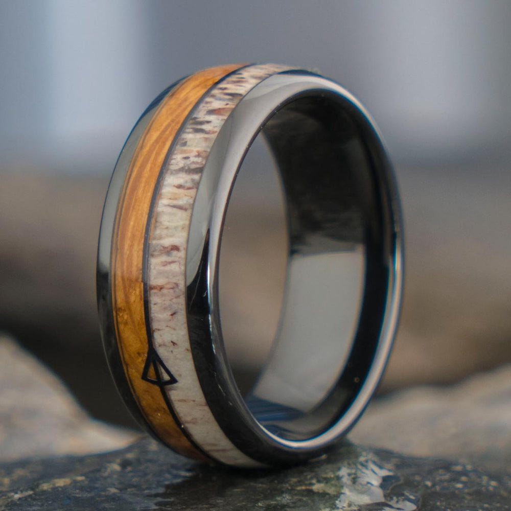 The Guardian black tungsten ring with whiskey barrel wood, antler inlay, and arrow detail. Product shot.