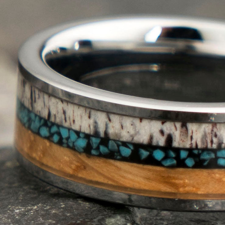 The Dassault tungsten ring with whiskey barrel, antler, and turquoise inlay on a dark surface.