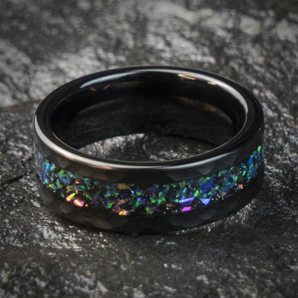 Black hammered tungsten wedding band with blue, green, and purple starry sky opal inlay on dark textured surface.