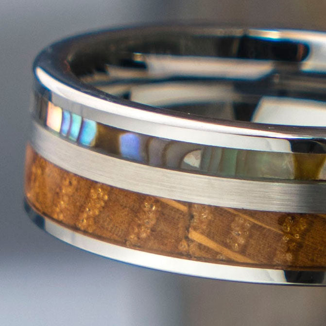 Close-up of Mercury tungsten wedding band featuring whiskey barrel wood inlay and iridescent abalone shell stripe.