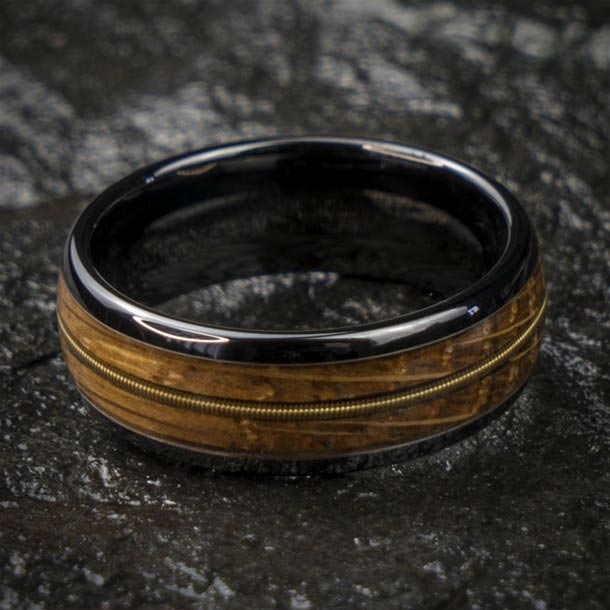 Black ceramic ring with whiskey barrel wood inlay and guitar string detail, showcasing unique craftsmanship.